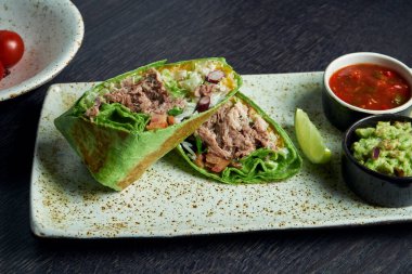 Sığır eti, pirinç, domates, mısır ve dolmalık biberli burritoyu kahverengi bir tabakta domates sosu ve guacamole ile yakın çekim yapın. Vejetaryen Shawarma Roll