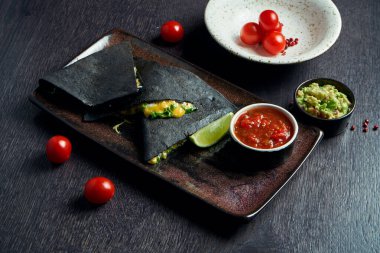 Yakın plan siyah tortilla quesadilla peynirli kahverengi tabakta ahşap arka planda kırmızı sos. Meksika geleneksel mutfağı.