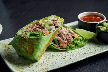 Sığır eti, pirinç, domates, mısır ve dolmalık biberli burritoyu kahverengi bir tabakta domates sosu ve guacamole ile yakın çekim yapın. Vejetaryen Shawarma Roll