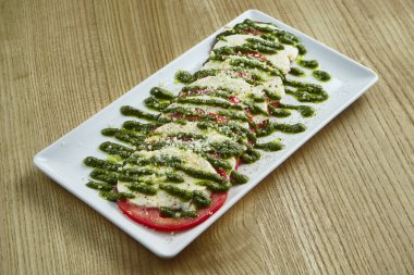 İştah açıcı İtalyan caprese salatasına yakından bakın. Taze domatesler, yumuşak mozzarella, roka ve kırsal arka planda beyaz bir tabakta pesto sosu. Sağlıklı yemek.