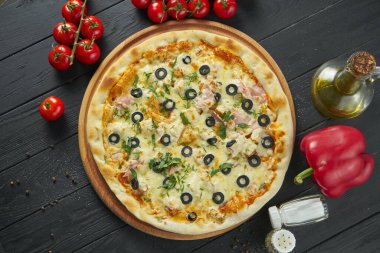 Eritilmiş peynirli, tavuklu, jambonlu ve zeytinli iştah açıcı pizzayı yakın çekim bir restoranda koyu ahşap arka planda. Pizza kompozisyonu. İtalyan mutfağı. Yemek düzdü.