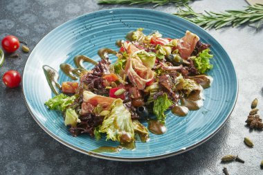 Jambonlu iştah açıcı salata, marul, zeytin ve koyu arkaplanda mavi seramik tabakta tatlı sos. Görüntüyü kapat