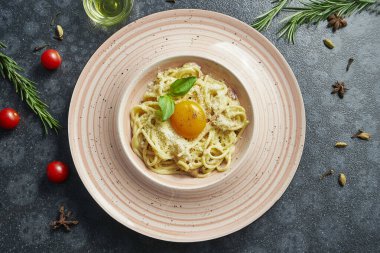 Ev yapımı ve sarısı ve parmesanlı taze carbonara makarnası. Siyah arka planda pembe bir tabakta, içinde malzemeler olan İtalyan iştah açıcı spagetti.
