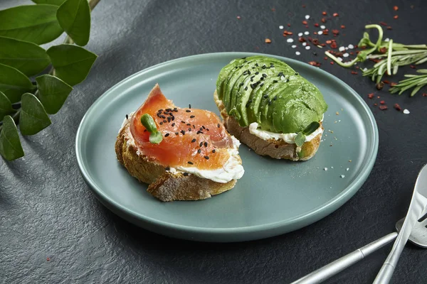 Trendy street snack. Tasty sandwich toast with salmon and avocado on craft paper on a black background. Top view. Flay lay food with copy space. Seafood