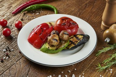 Izgara sebzeler: domates, orman mantarları, ahşap arka planda beyaz bir tabakta sosla tatlandırılmış kabak. Lezzetli ve dengeli vejetaryen yemekleri..