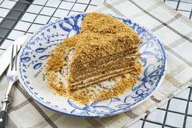 Katmanlı ballı pasta ve beyaz arka planda seramik tabakta kremalı pasta. Bir dilim lezzetli Medovik keki. Kapatın. Lezzetli fırın konsepti. Seçici odak