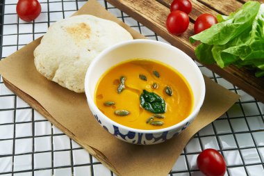 Beyaz arka planda parşömen üzerinde servis edilen seramik fiyonklu Focaccia çöreği ile lezzetli balkabağı kremalı çorbanın manzarasını kapatın.