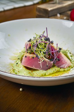 Lezzetli iştah açıcı salata, orta pişmiş ton balığı, kapari, vişneli domates, ahşap arka planda beyaz bir tabakta kuşkonmaz.