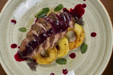 Ahşap bir arka planda beyaz bir tabakta ananas ve tatlı böğürtlen soslu lezzetli fırında ördek filetosunun yakın görüntüsü. Şenlikli bir akşam yemeği için lezzetli et..