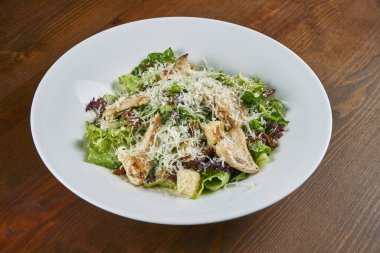 Ceasar salatası, kızarmış ekmek, parmesan, tavuk, yumurta ve beyaz bir kase. Restoran servisi. Seçici odak, tahta arkaplan