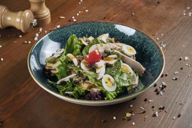 Lezzetli, taze salata, ördek göğsü, ıspanak, kinoa, bıldırcın yumurtası ve ahşap arka planda mavi bir kasede kiraz domatesleri. Sağlıklı Zindelik Beslenme. Yemeği kapat.