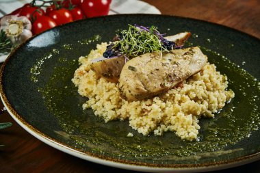 Kuskus garnitürlü tavuk filetosu ve ahşap arka planda yeşil bir kasede pesto sosu. Diyet fitness beslenmesi. Sağlıklı yiyecekler. Görüntüyü kapat