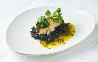 Izgara turna balığı, sarımsaklı, siyah pirinç ve mango sosuyla süslenmiş, beyaz bir tabakta, ahşap bir zemin üzerinde. Lezzetli deniz ürünleri yemeğinin manzarasını kapat.