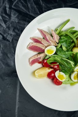 Lezzetli iştah açıcı salataya yakından bakın orta pişmiş ton balığı, kapari, vişneli domates, siyah arka planda beyaz tabakta kuşkonmaz.