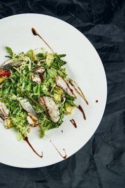 Kızarmış levrek, ıspanak, marul ve siyah arka planda vişneli domatesle servis edilen gurme salatası. Lezzetli deniz ürünleri salatası. Sağlıklı yiyecekler. Diyet ve zindelik beslenmesi