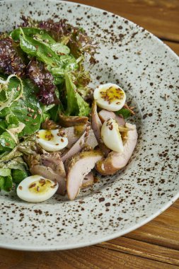 Lezzetli, taze salata, ördek göğsü, ıspanak, kinoa, bıldırcın yumurtası ve kiraz domatesleri ahşap arka planda beyaz bir kasede. Sağlıklı Zindelik Beslenme. Yemeği kapat.