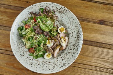 Lezzetli, taze salata, ördek göğsü, ıspanak, kinoa, bıldırcın yumurtası ve kiraz domatesleri ahşap arka planda beyaz bir kasede. Sağlıklı Zindelik Beslenme. Yemeği kapat.