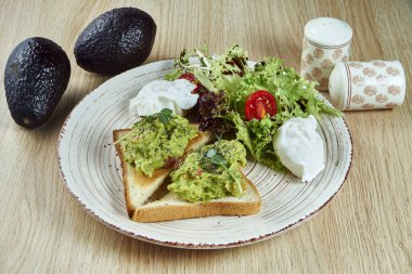 Avokado guacamole ile sunulan kızarmış yumurta ve marulla birlikte beyaz, seramik bir tabakta ahşap bir zemin. Modern Meksika mutfağı. Lezzetli yiyeceklere yakından bakın.