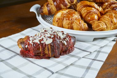 Üç yeni pişmiş kruvasan ve ahşap bir arka planda bej kumaş üzerine çilek ve boğaz. Fırın kafeleri için yemek fotoğrafçılığı. Görüntüyü kapat.
