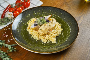 Kuskus garnitürlü tavuk filetosu ve ahşap arka planda yeşil bir kasede pesto sosu. Diyet fitness beslenmesi. Sağlıklı yiyecekler. Görüntüyü kapat