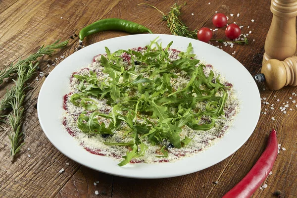 Parmesan, roka ve trüf yağlı dana carpaccio beyaz bir tabakta ahşap arka planda İtalyan mutfağında baharatlarla bezenmiş. Salata, antipasti.