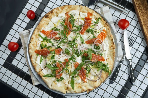 Tasty pizza with cheese, cherry tomatoes, salmon, arugula and parmesan on a wooden background. Italian traditional cuisine. Top view. Food for lunch