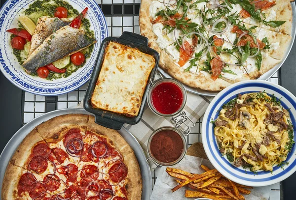 Italian dining table with pizza, pasta, baked sea bass, lasagna and desserts.. Top view food flat lay.