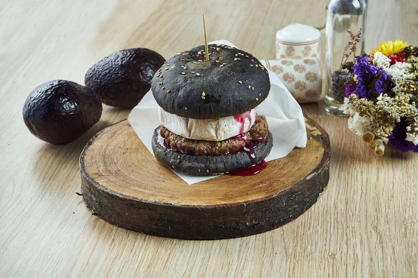 Tasty, juicy burger with a black bun with camembert, cranberry sauce and beef on a wooden board. Fast-food. Close up. Copy space.