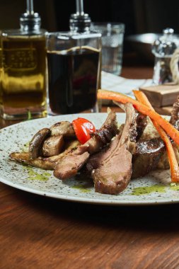 Sebzeli ve beyaz tabakta yeşil makarna ile sulu bir kuzu pirzolası. Restoran şeften servis. Ahşap arka plan. Yaklaş, seçici odaklanma. Yemek düzdü.