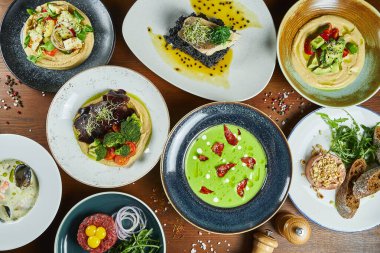 Bir sürü yiyecekle birlikte yemek masası. Aile yemeği için yeşil kremalı çorba, humus, dorado, pate, bouillabaisse ve sığır etli tartar. Üst manzaralı yiyecek düzlüğü.