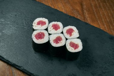 Suşi maki ahşap bir arka planda siyah tahtada ton balıklı rulo yapar. Japon mutfağı. Kapat.