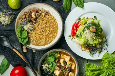 İçinde vejetaryen yemekleri olan bir yemek masası kompozisyonu: mantarlı risotto, taze salata ve gri bir bez üzerinde miso çorbası. Sağlıklı ve dengeli yiyecekler. Menü fotoğrafı, üst görünüm