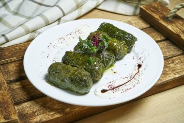 Traditional georgian dolma in grape leaves staffed with rice and meat on white plate on wooden background. CLose up. Selective focus. clipart