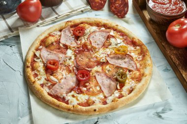 Domatesli, peynirli, jambonlu, kırmızı soslu ev yapımı et pizzası. Çıtır pizzalı kompozisyon, arka planda domatesler. Uzayı kopyala Üst görünüm
