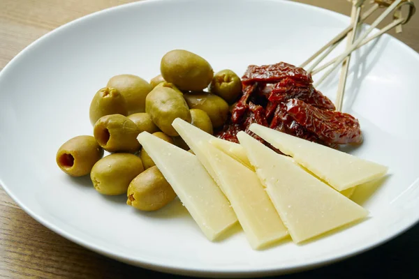 Snacks for dinner. Antipasti plate with olives, hard cheese and sun-dried tomatoes. close up view