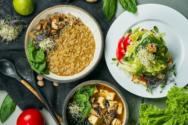 Composition with a dinner table with vegetarian dishes: risotto with mushrooms, fresh salad and miso soup on a gray cloth. Healthy and balanced food. Menu photo, top view