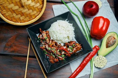 Klasik bir Asya yemeği. Ahşap bir arka planda siyah tabakta teriyaki kızarmış domuz tavası ile pilav. Kapat.