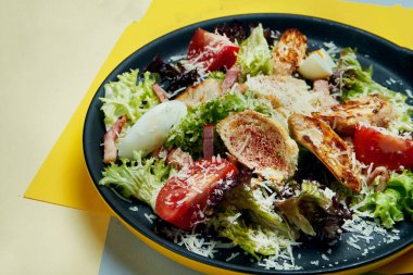 Ceasar salatası, kızarmış ekmek, parmesan, tavuk, siyah tabakta siyah arka planda yumurta. Restoran servisi. Kapat.