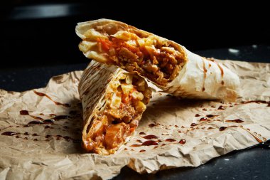 Et, salata ve ev yapımı sos ile nefis shawarma dürümü. Siyah arka plandaki el işi kağıdında ince pide ekmeği. Doğu mutfağı. Izgara etle dilimlenmiş kebap..