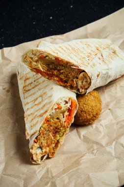 Falafel, salata ve ev yapımı sos ile nefis shawarma dürümü. Siyah arka planda ince pide pişmiş ekmek. Doğu mutfağı. Falafel ile dilimlenmiş kebap..