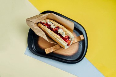 Karamelli soğanlı klasik Amerikan sosislisi, çedar peyniri, hardal ve yanında renkli arkaplanda patates olan ketçap. Fast food