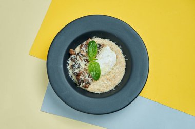 Lezzetli ve sağlıklı bir kahvaltı. Yağda yumurta, parmesan ve mantarlı yulaf ezmesi renkli arka planda siyah bir tabakta.