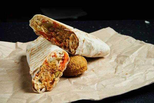Falafel, salata ve ev yapımı sos ile nefis shawarma dürümü. Siyah arka planda ince pide pişmiş ekmek. Doğu mutfağı. Falafel ile dilimlenmiş kebap..