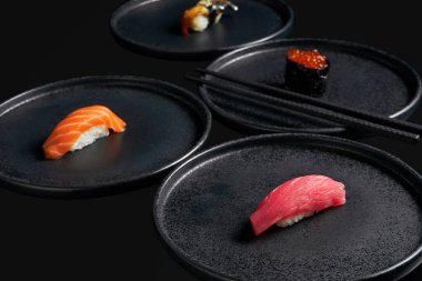 Ton balıklı saşimi suşi, somon havyarı, somon balığı ve füme yılan balığını siyah arka planda şık siyah seramik tabaklara koyun. Geleneksel Japon mutfağı. Menü için fotoğraf