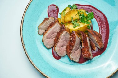 Gri arkaplanda izole edilmiş mavi bir tabakta çilek soslu ve elmalı iştah açıcı fırınlanmış ördek filetosu. Kapat..