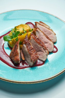 Gri arkaplanda izole edilmiş mavi bir tabakta çilek soslu ve elmalı iştah açıcı fırınlanmış ördek filetosu. Kapat..