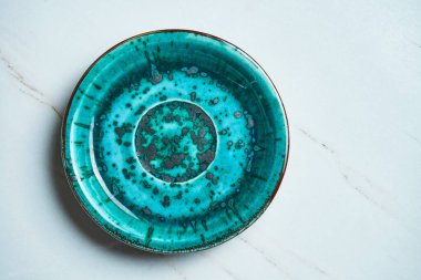 Gri mermer bir zeminde el yapımı boş mavi seramik tabağın üst görüntüsü. Uzayı metin için kopyala. Şık mutfak aletleri