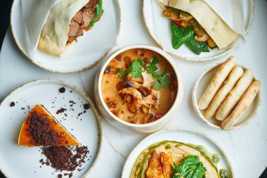 Çok çeşitli yemekleri olan yemek masası. Et, humus, deniz ürünleri çorbası ve mermer arka planda peynirli kek. Üst manzara, yemek düzlüğü