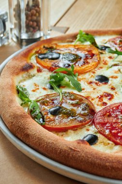 Eritilmiş peynirli iştah açıcı pizza ve ahşap zemin üzerinde çıtır çıtır kabuklu farklı domatesler. Restoran servisi. Pizza Margherita.