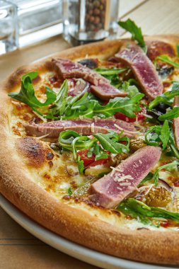 Ton balığı, roka, vişneli domates ve ahşap zemin üzerinde çıtır çıtır parmesanlı iştah açıcı pizza. Restoran servisi. Deniz ürünleri pizzası.